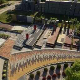 Firma Barabaś Sp. z o.o. - Ekspozycja różnorodnych wzorów kostki brukowej i granitowej na zewnątrz, z paletami kostki w tle. Widok z góry prezentuje bogactwo kolorów i faktur.