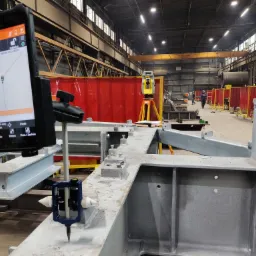 Pomiar konstrukcji stalowej za pomocą tachimetru i tabletu z oprogramowaniem geodezyjnym na hali produkcyjnej.