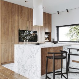INTUS GROUP - Nowoczesna kuchnia z drewnianymi szafkami, wyspą z marmurowym blatem i czarnymi stołkami barowymi; cylindryczny okap nad wyspą, drewniana podłoga.