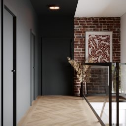 INTUS GROUP - Nowoczesny korytarz z parkietem w jodełkę, ceglaną ścianą z abstrakcyjnym obrazem, czarnymi drzwiami i szarą ścianą z białymi listwami.