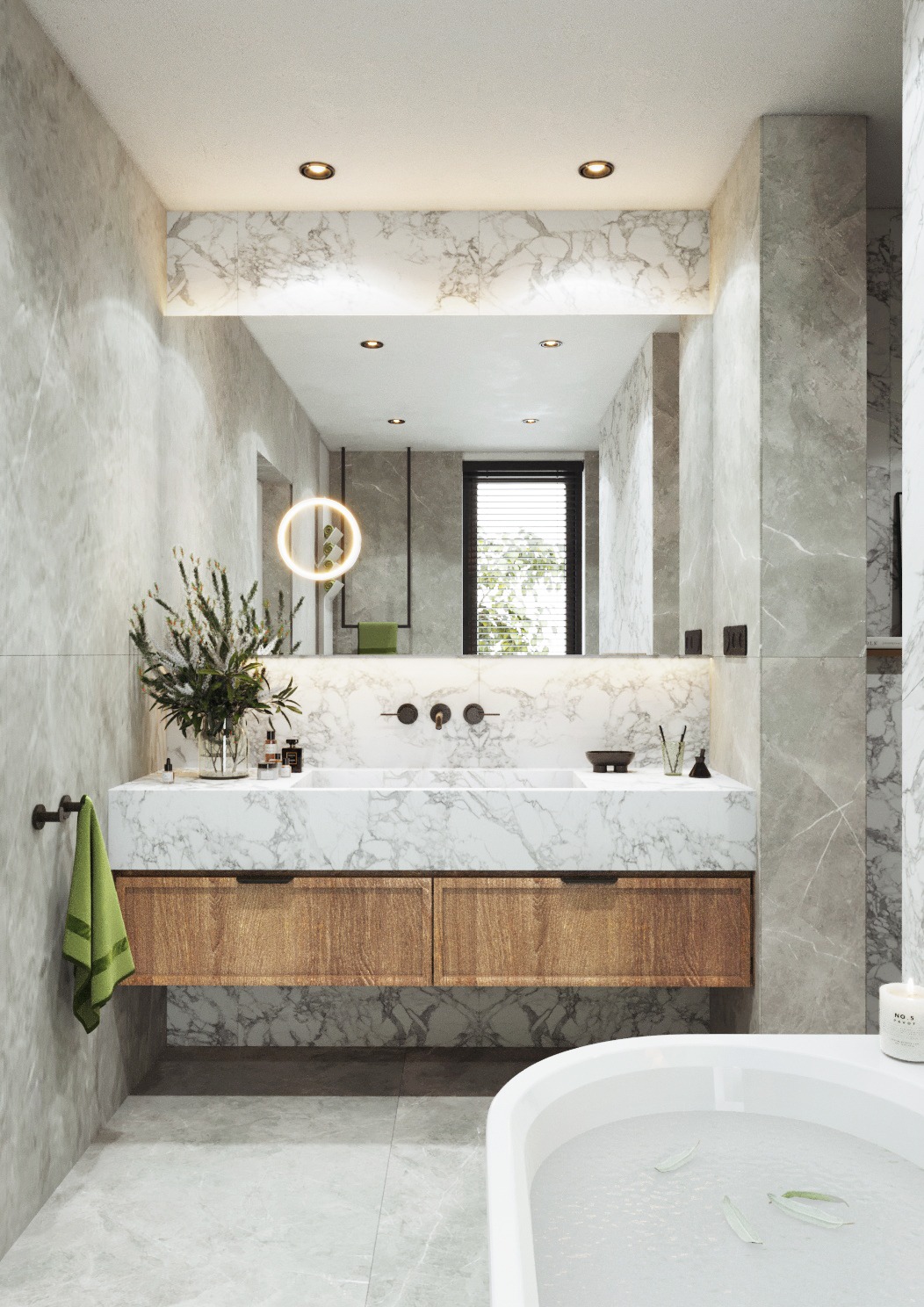 Nowoczesna łazienka z marmurowymi ścianami i blatem umywalki, drewniane szafki pod umywalką, okrągłe lustro z podświetleniem oraz biała wanna z płatkami kwiatów.