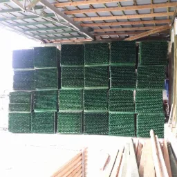 Magazynowane, impregnowane ciśnieniowo, zielone drewno konstrukcyjne w wiązkach pod zadaszeniem, widoczne elementy więźby dachowej.