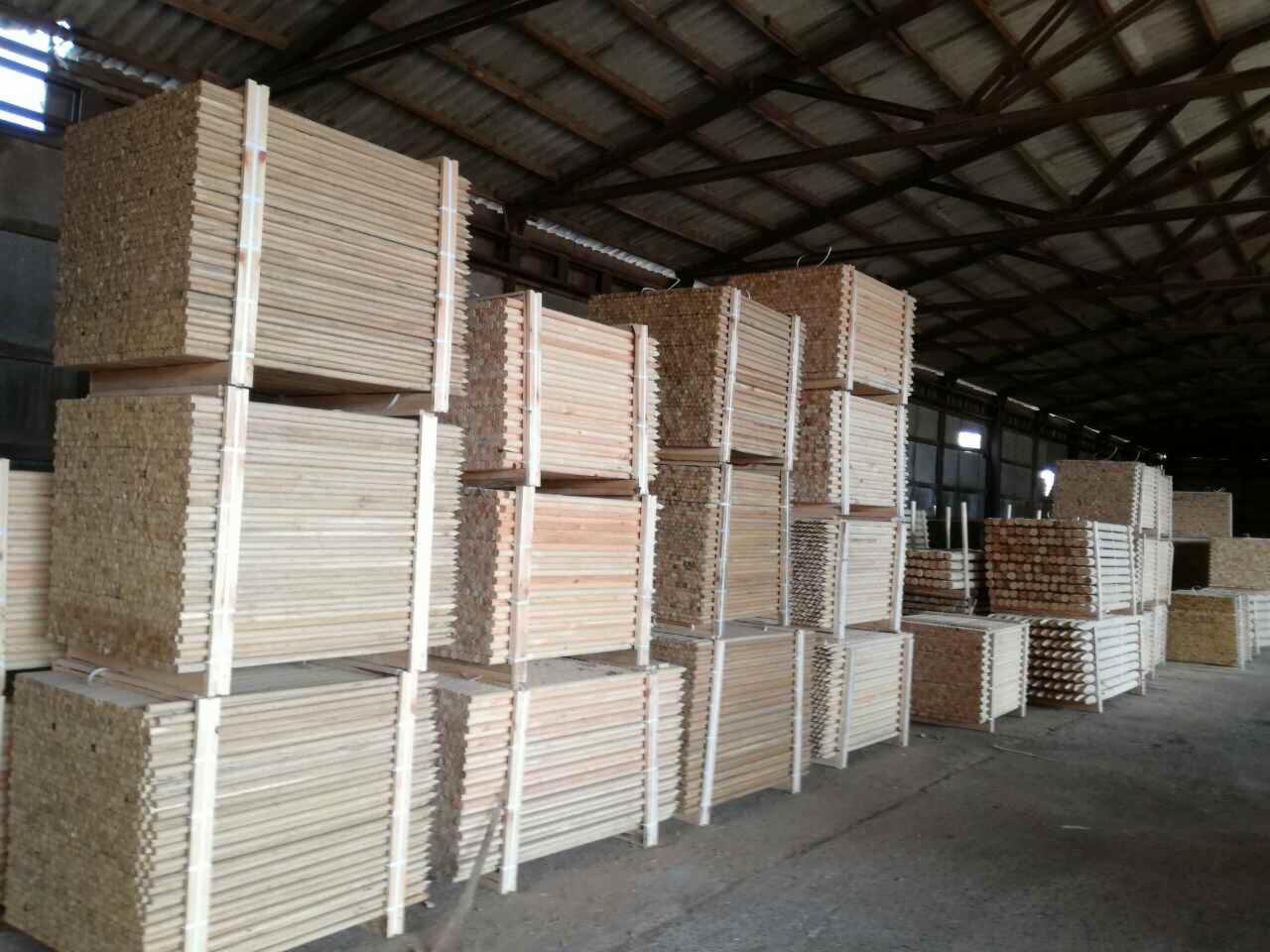 Magazyn z ułożonymi w stosy paczkami świeżo przetartego drewna budowlanego, zabezpieczonymi białymi taśmami.
