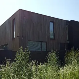 Nowoczesny dom jednorodzinny z drewnianą elewacją w pionowym układzie, z elementami w kolorze czarnym, otoczony zielenią.