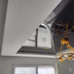 Nowoczesny, wielopoziomowy sufit z podwieszaną konstrukcją i wbudowanym oświetleniem, zabezpieczony folią malarską podczas prac wykończeniowych, z widoczną designerską lampą wiszącą.