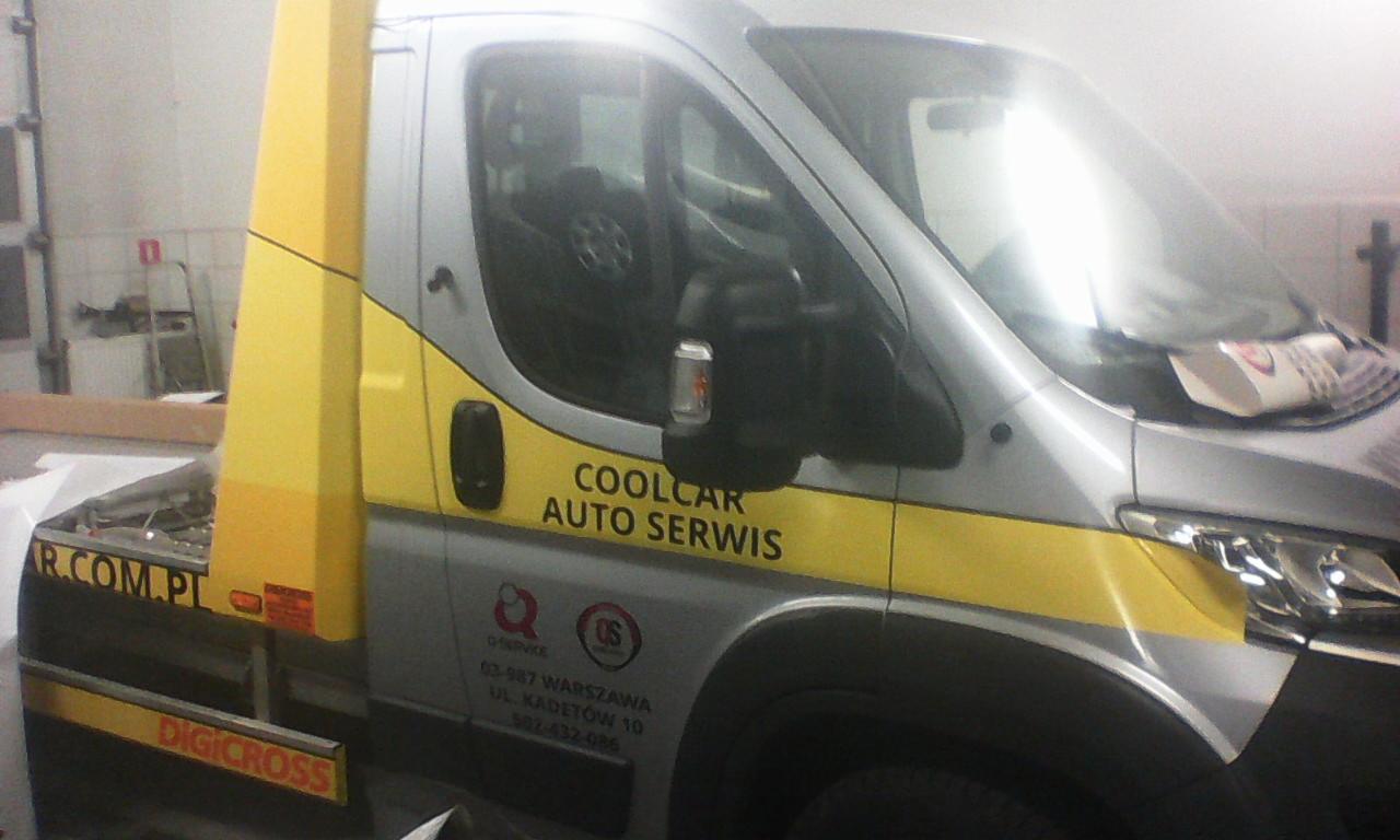 Srebrny bus z żółtymi naklejkami 'COOLCAR AUTO SERWIS' i 'DIGICROSS', zaparkowany w warsztacie. Widoczne dane adresowe i logo firmy.