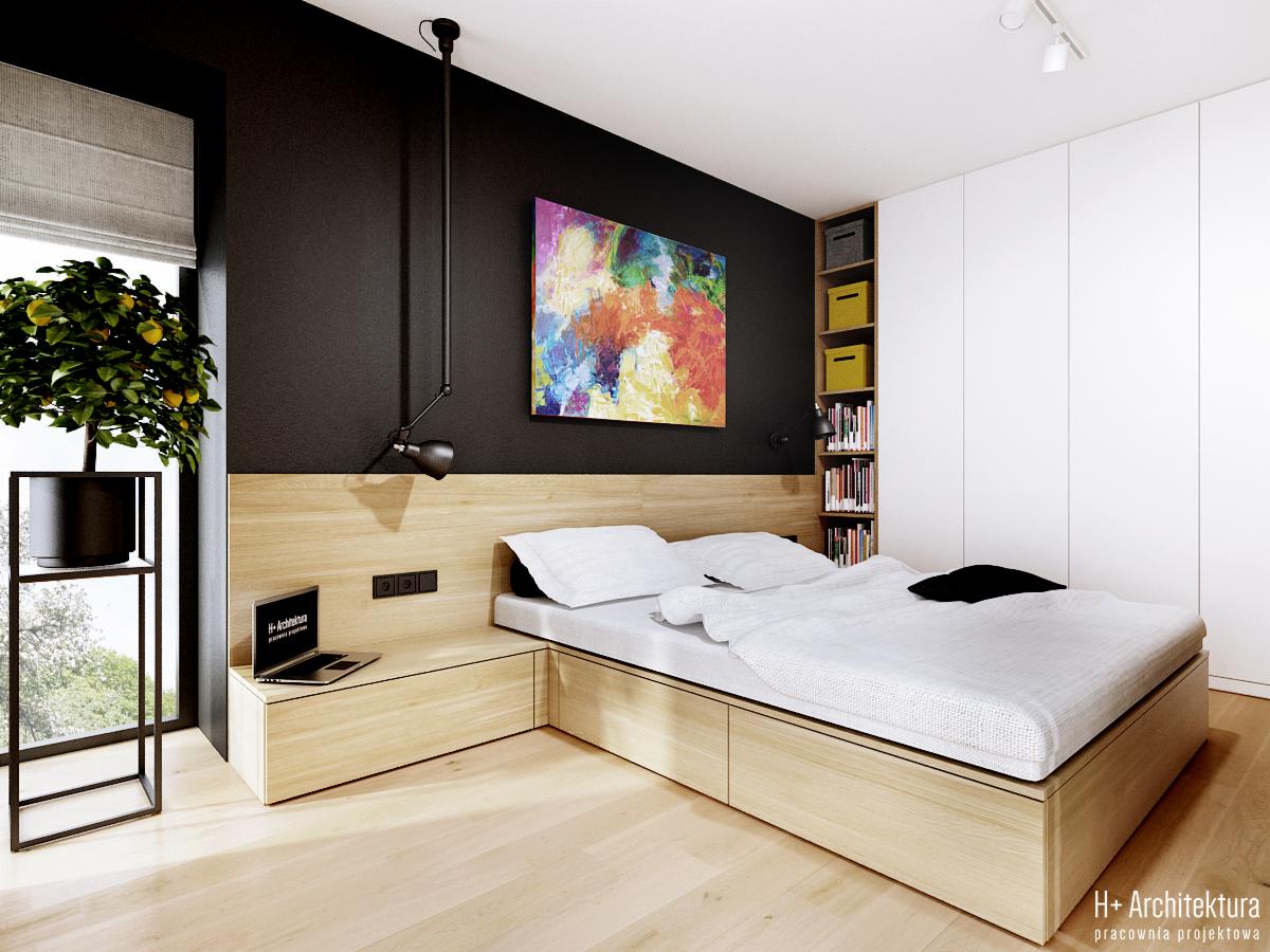Nowoczesna sypialnia z drewnianym łóżkiem z szufladami, czarną ścianą z kolorowym obrazem, minimalistyczną lampą i rośliną w doniczce przy oknie. Na łóżku biała pościel i czarna poduszka. Na szafce...