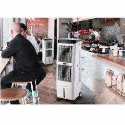 PanKlimatyczny.pl sklep internetowy - Klimatyzatory przenośne z logo producenta w kawiarni z klientami siedzącymi przy stolikach. Jeden klimatyzator stoi blisko lady z deserami i napojami.