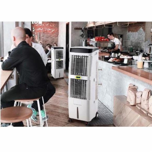 Klimatyzatory przenośne z logo producenta w kawiarni z klientami siedzącymi przy stolikach. Jeden klimatyzator stoi blisko lady z deserami i napojami.