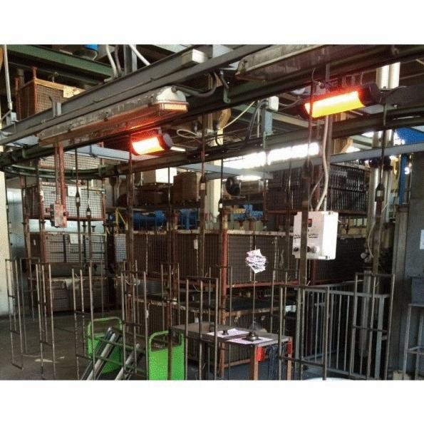 Dwa przemysłowe promienniki ciepła zamontowane pod sufitem w hali produkcyjnej, oświetlające metalowe konstrukcje i wózki transportowe.