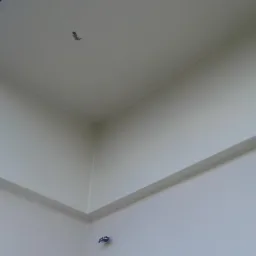 Świeżo pomalowany narożnik elewacji zewnętrznej budynku z widocznym elementem wentylacyjnym w suficie.