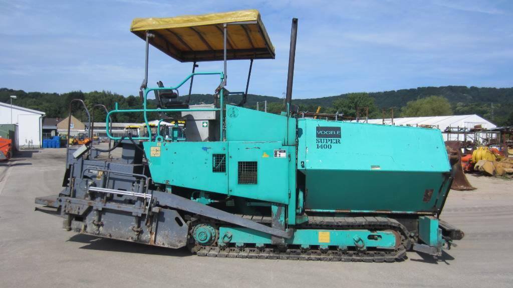 Rozściełacz VOGELE SUPER 1400 na gąsienicach, widoczny z boku, z żółtym daszkiem i zielono-turkusową karoserią, stojący na placu budowy.