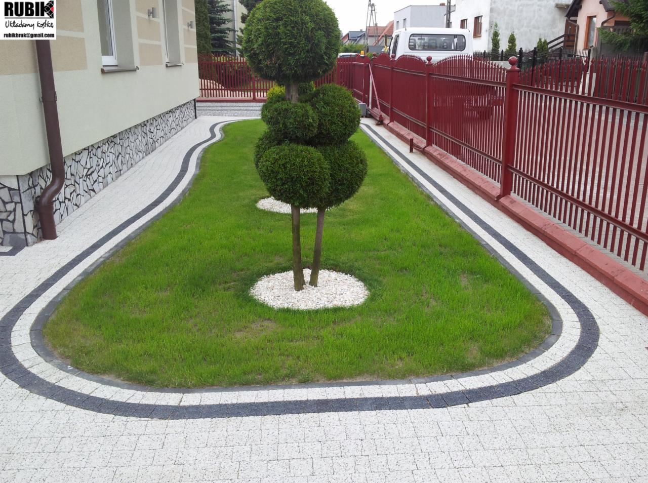 Ogród z kostki brukowej w Bobowo: elegancki chodnik z obrzeżem, trawnik z formowanymi drzewkami i czerwone ogrodzenie. Estetyczne wykończenie posesji.