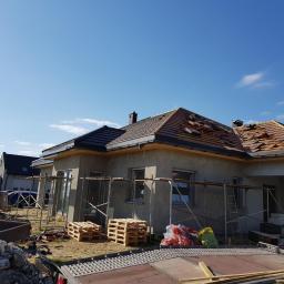 Firma Remontowo Budowlana - Dekarstwo Rafał Cichy - Dom w trakcie wymiany pokrycia dachowego: część dachu z nową, czarną dachówką, druga część zdemontowana, widoczne rusztowania i materiały budowlane.