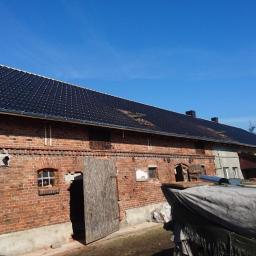 Firma Remontowo Budowlana - Dekarstwo Rafał Cichy - Częściowo wymieniony dach z czarnej dachówki na ceglanym budynku gospodarczym z widocznymi śladami wcześniejszych prac dekarskich.