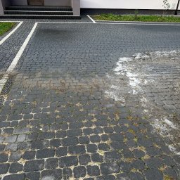 Quoss Agnieszka Sidor - Częściowo umyta, czarna kostka brukowa przed domem w Wojciechowie, z widocznymi smugami wody i resztkami piany po czyszczeniu, kontrastująca z suchą częścią nawierzchni.