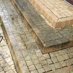 Quoss Agnieszka Sidor - Schody z kostki brukowej częściowo umyte, widoczna różnica w kolorze między czystą a brudną powierzchnią, zarys okna w tle.