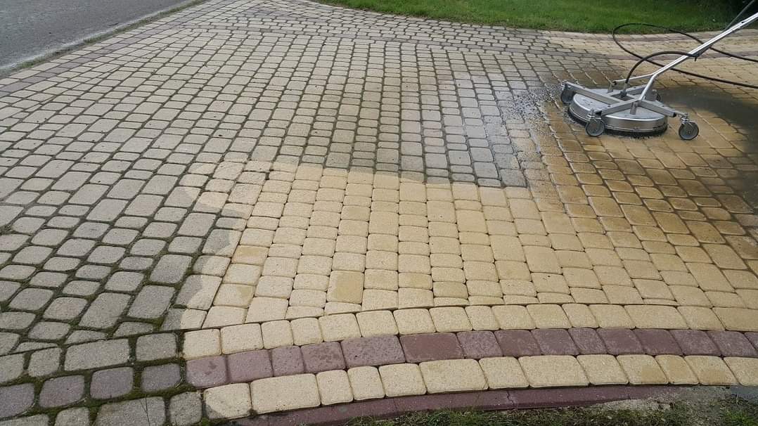 Czyszczenie kostki brukowej wielokolorowej myjką ciśnieniową z okrągłą dyszą, widoczna różnica w kolorze między czystą i brudną powierzchnią.