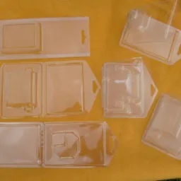 Różne przezroczyste plastikowe wytłoczki, niektóre z otworami do zawieszania, ułożone na żółtym tle.