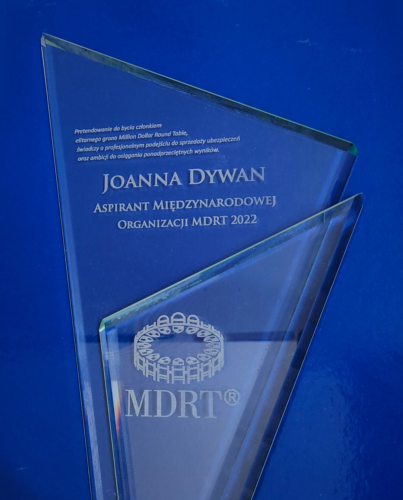 Szklana statuetka MDRT dla Joanny Dywan, aspiranta międzynarodowej organizacji z 2022 roku, symbolizująca profesjonalizm w sprzedaży ubezpieczeń.