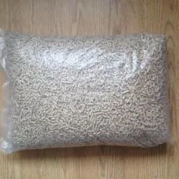 Worek przezroczysty wypełniony jasnymi, drobnymi granulkami pelletu, leżący na podłodze imitującej drewno, z fragmentem czarnego buta w prawym górnym rogu.