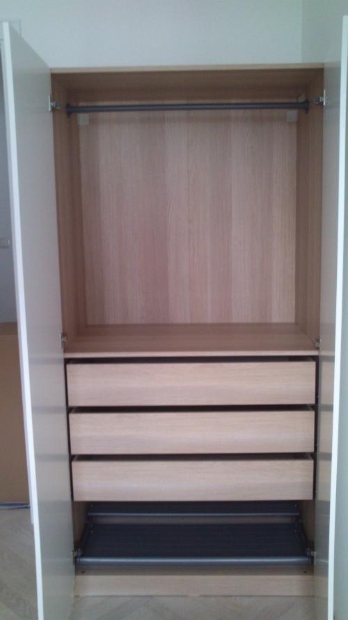 Wnętrze szafy z jasnego drewna z trzema szufladami i drążkiem na ubrania, widok z otwartymi drzwiami.