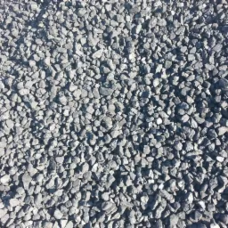 Szare bryłki ekogroszku o nieregularnych kształtach, oświetlone z góry, tworzące jednolitą powierzchnię.