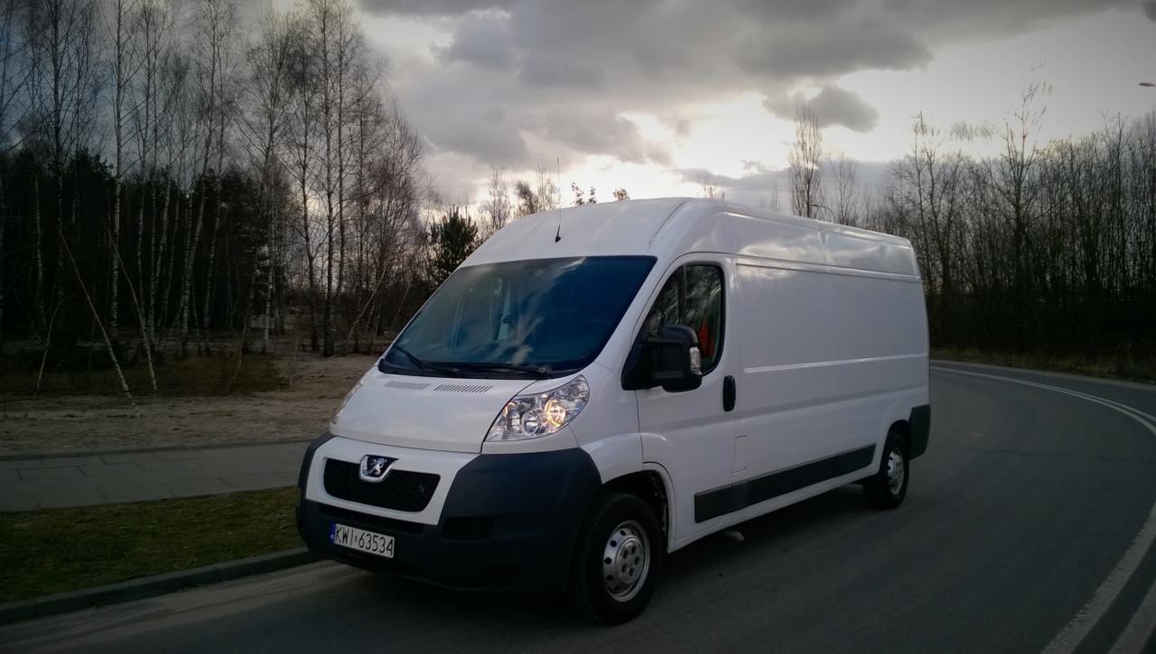 Biały bus Peugeot na poboczu drogi, jesienne drzewa w tle, pochmurne niebo. Widoczna tablica rejestracyjna. Idealny do transportu.
