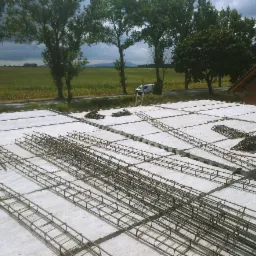 Przygotowanie zbrojenia na stropie Teriva z widocznymi belkami i pustakami, w tle krajobraz polny i samochód dostawczy.