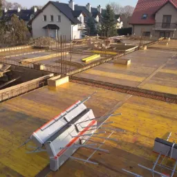 Żółte szalunki stropowe zbrojone stalą na budowie domu jednorodzinnego, widok z góry na konstrukcję w trakcie realizacji.