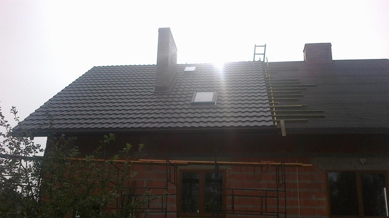 Częściowo pokryty dach blachodachówką z oknami dachowymi i kominem. Na fragmencie dachu widoczne łaty pod pokrycie. Budynek w trakcie budowy.