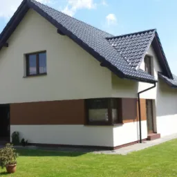 Elewacja domu jednorodzinnego z jasnym tynkiem i poziomym pasem z paneli drewnopodobnych, ciemna dachówka, zadbany trawnik