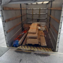 Wnętrze przestrzeni ładunkowej busa wypełnione kartonami i zabezpieczone pasami transportowymi, widok z rampy załadunkowej.