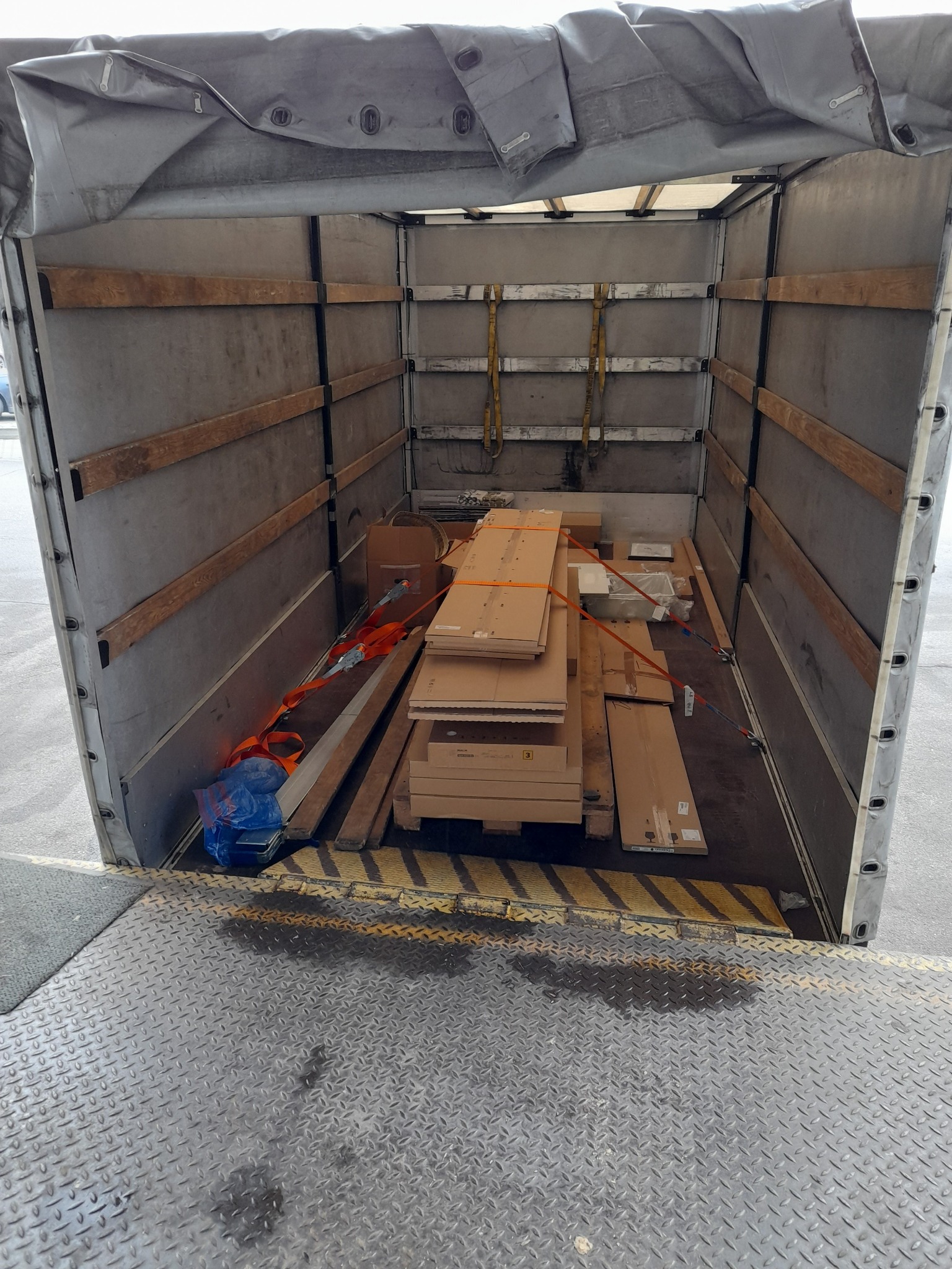 Wnętrze przestrzeni ładunkowej busa wypełnione kartonami i zabezpieczone pasami transportowymi, widok z rampy załadunkowej.