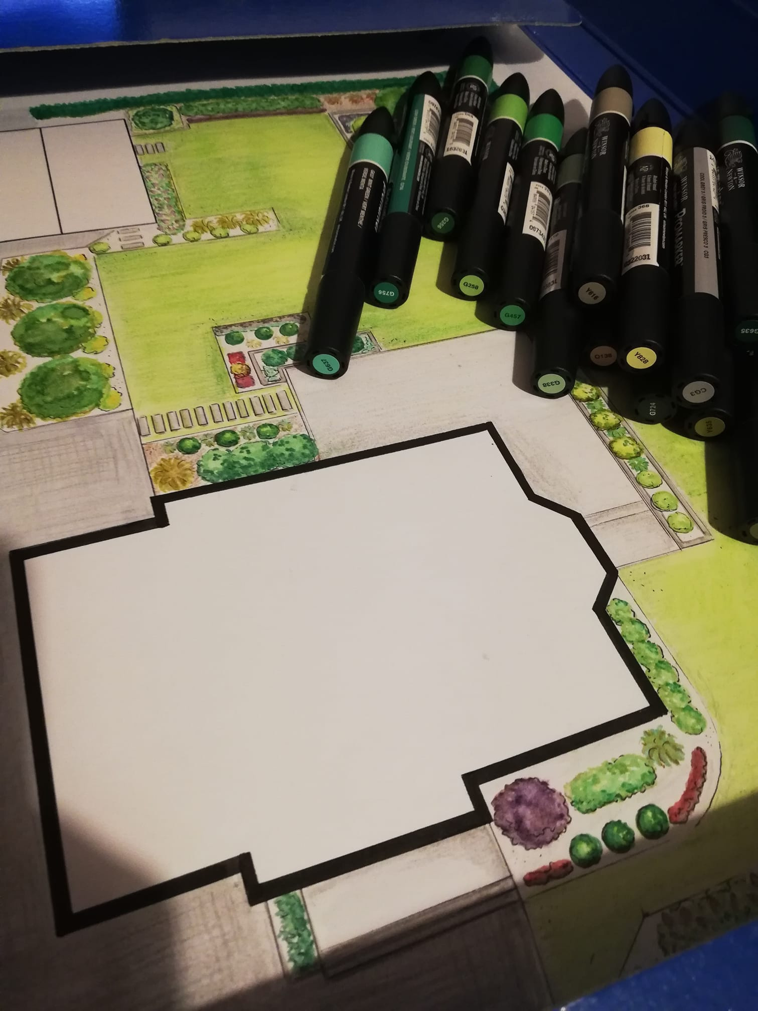 Ręcznie rysowany plan zagospodarowania terenu z zaznaczonym budynkiem i zielenią, uzupełniony o zestaw markerów w odcieniach zieleni i żółci, sugerujący etap projektowania.