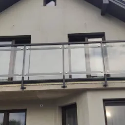 Balkon z nowoczesną balustradą ze szkła i czarnej stali, mocowaną na metalowych wspornikach, z widocznymi mocowaniami punktowymi.