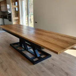 Rozkładany stół z drewnianym blatem i czarną, metalową podstawą o geometrycznym kształcie w nowoczesnym wnętrzu.