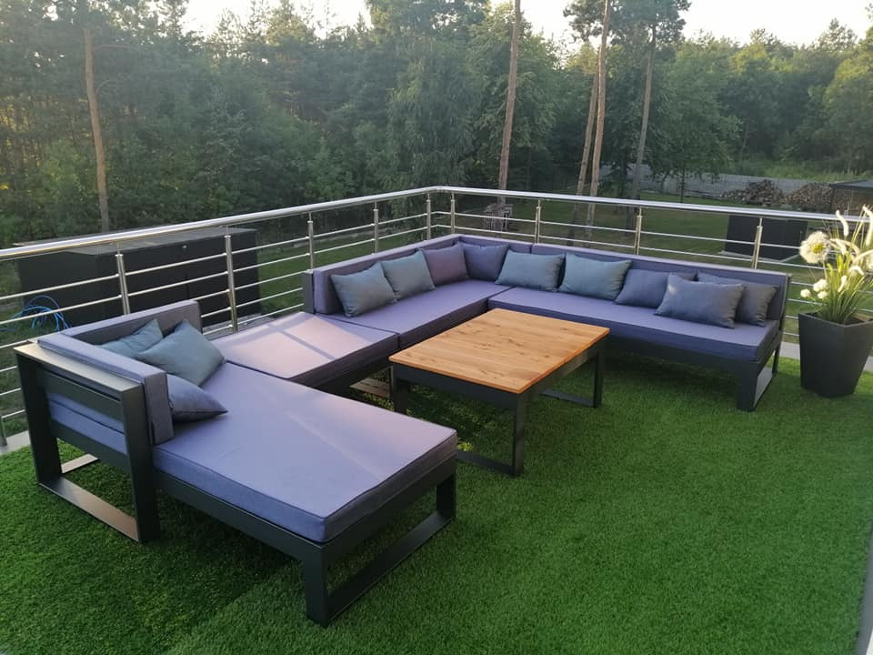 Narożny zestaw mebli ogrodowych z szarymi poduszkami na sztucznej trawie, otoczony balustradą ze stali nierdzewnej na tarasie.