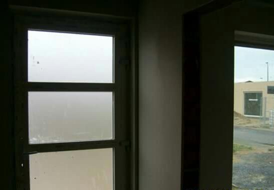 Surowe wnętrze z widokiem na zewnątrz przez okno, ściany przygotowane do tynkowania, widoczne niedoskonałości powierzchni.