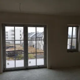 Wnętrze w stanie deweloperskim w Sosnowcu po nałożeniu tynków, widoczne okna z widokiem na budowę.