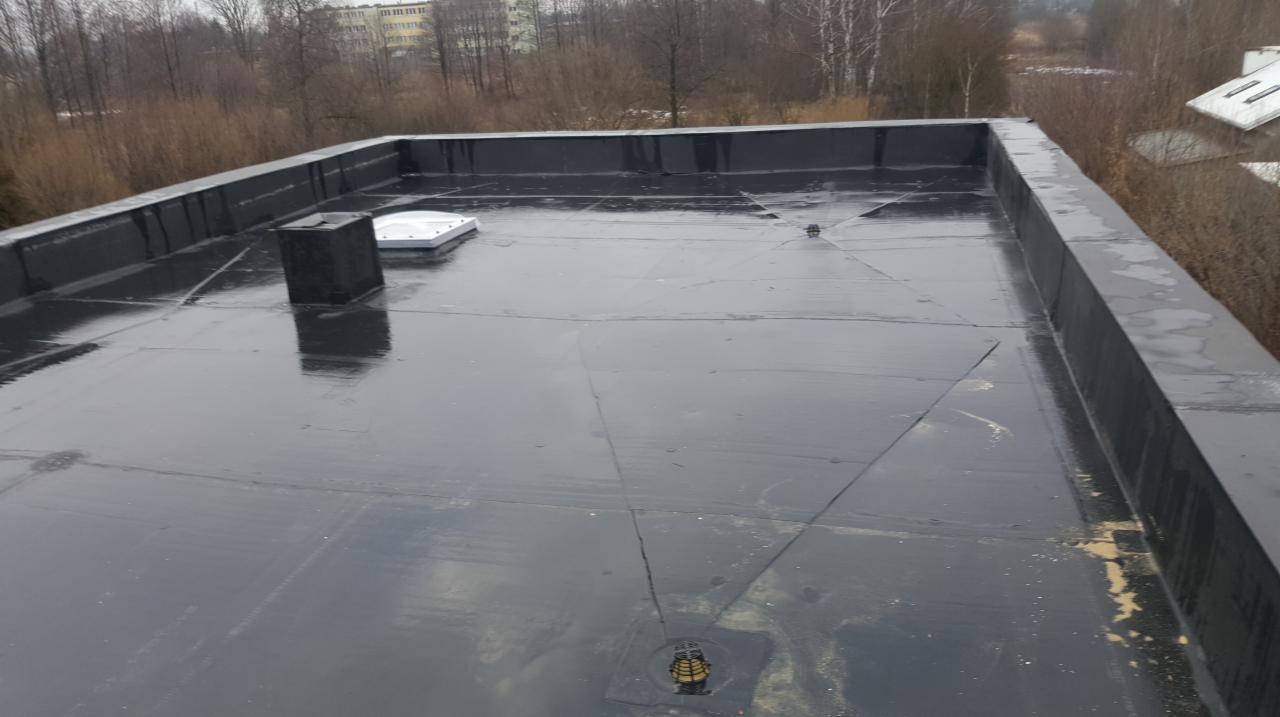 Płaski dach pokryty czarną membraną bitumiczną z kominem i świetlikiem w Bielsko-Białej, widoczny odpływ wody.