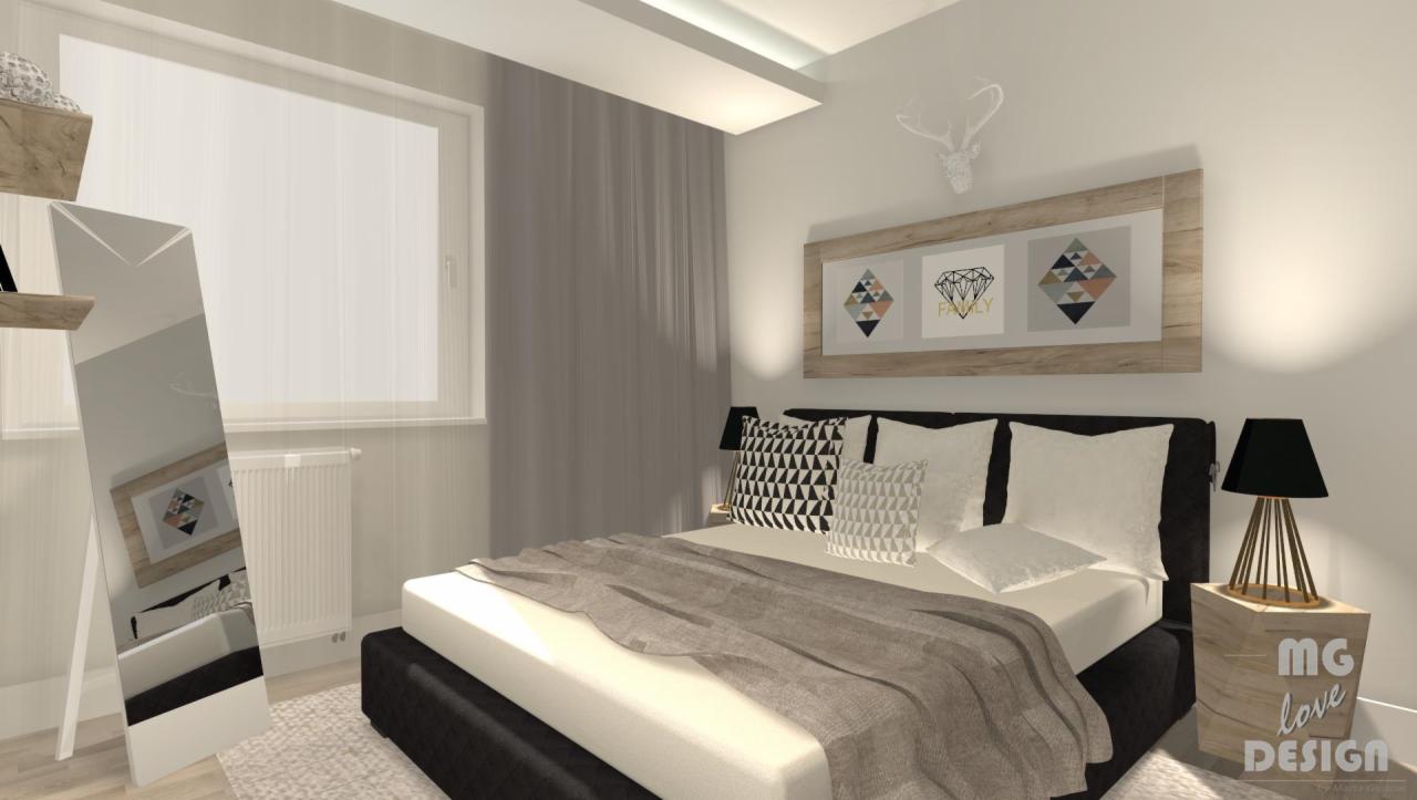 Nowoczesna sypialnia z łóżkiem kontynentalnym, geometrycznymi poduszkami i lustrem stojącym, odbijającym fragment pokoju. Nad łóżkiem rama z trzema grafikami w stylu skandynawskim.