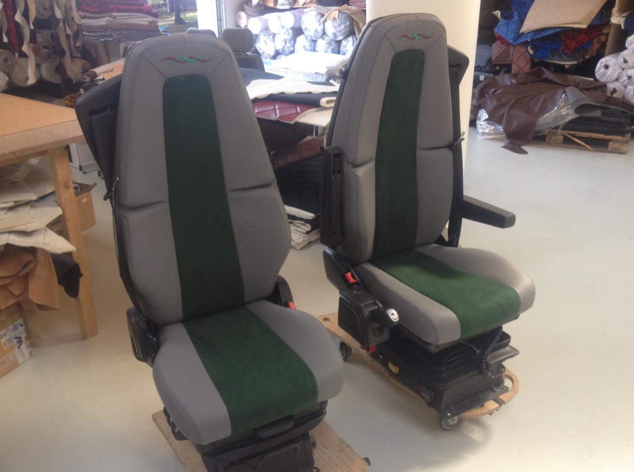 Dwa fotele samochodowe po renowacji tapicerskiej, szare z zielonymi wstawkami, widoczne w warsztacie z materiałami tapicerskimi w tle.