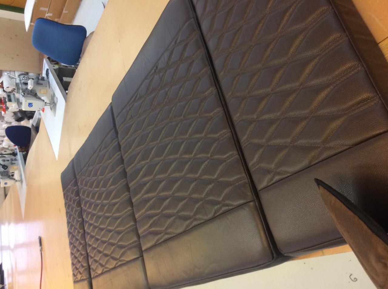 Brązowe, pikowane panele tapicerowane z ekoskóry na stole w warsztacie, widoczna maszyna do szycia i krzesło.