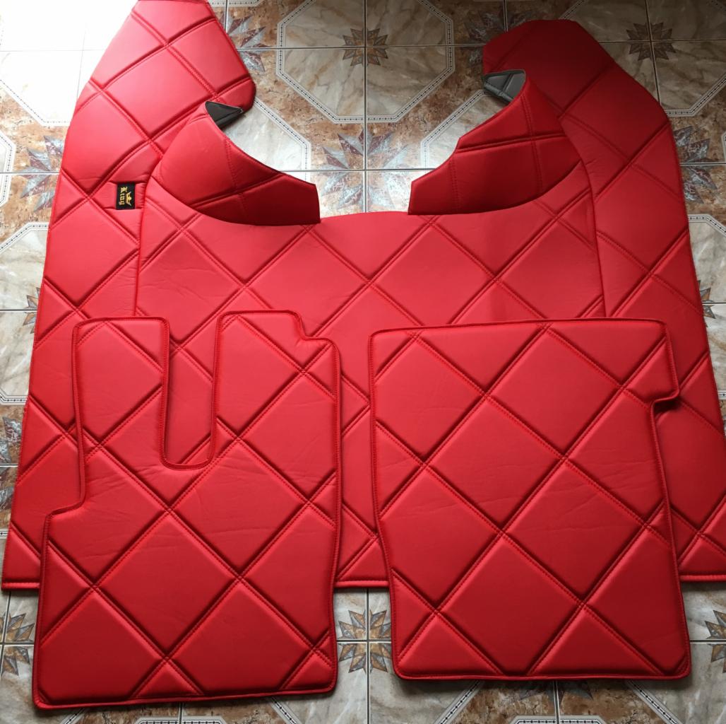 Czerwone, pikowane elementy tapicerki samochodowej, w tym dywaniki i panele boczne, ułożone na podłodze z płytek.