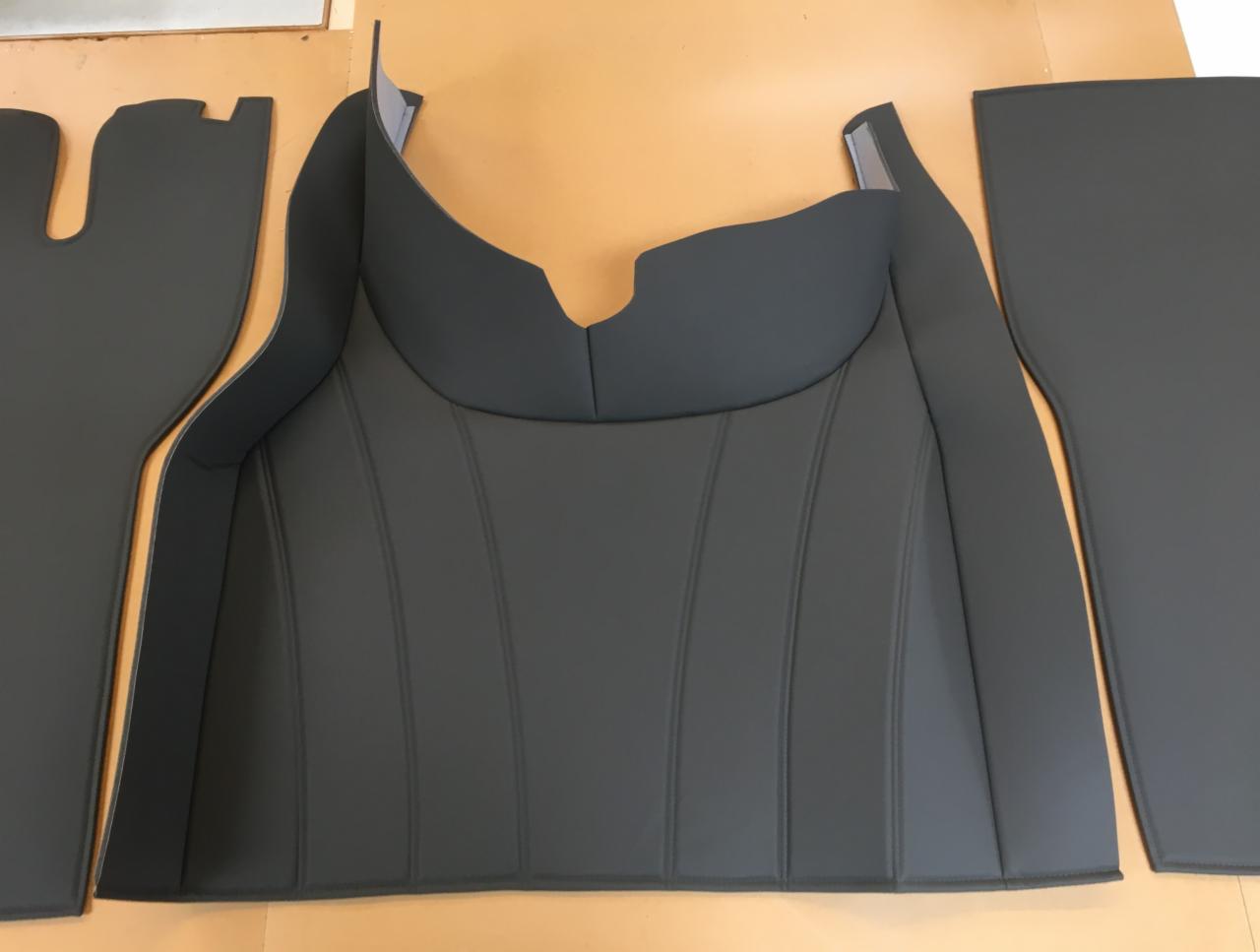 Elementy tapicerki samochodowej w odcieniach szarości, przygotowane do montażu, z widocznymi przeszyciami i krawędziami.