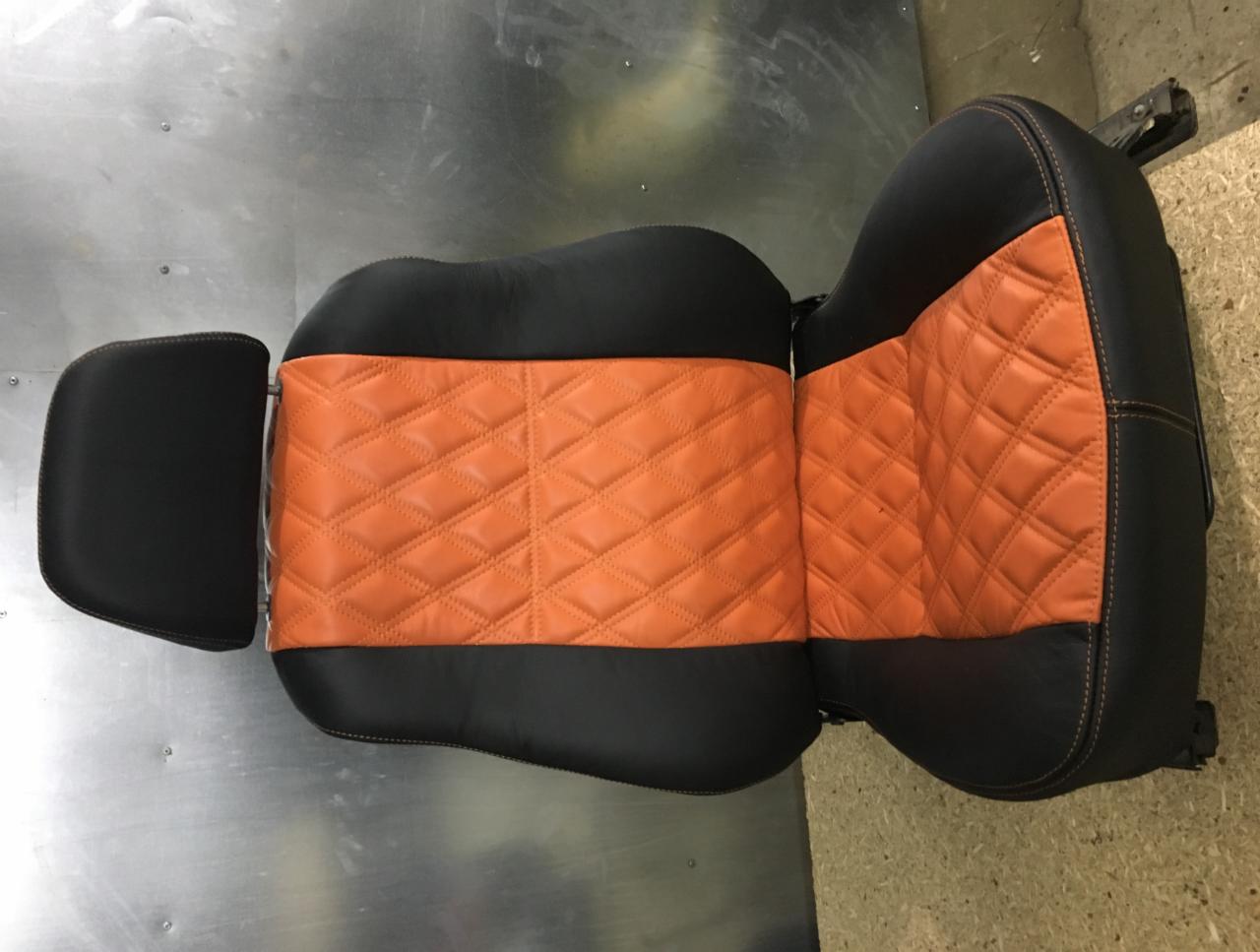 Odnowione, czarno-pomarańczowe skórzane siedzenie samochodowe z pikowanym wzorem diamentów, widoczne na metalowym stole.