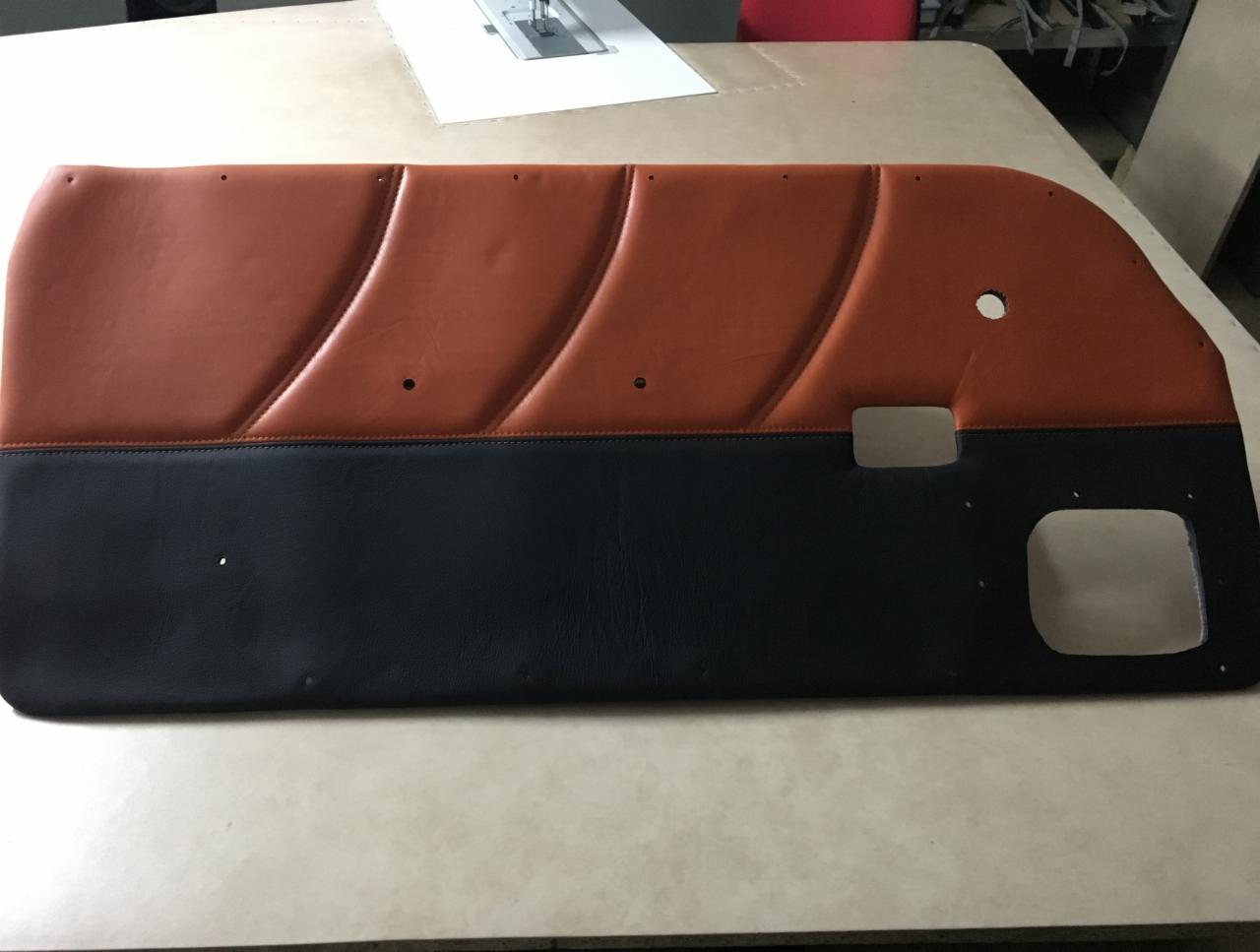 Tapicerowany panel drzwi samochodowych w kolorze brązowo-czarnym, z wyraźnymi przeszyciami i otworami montażowymi, leżący na stole w warsztacie.