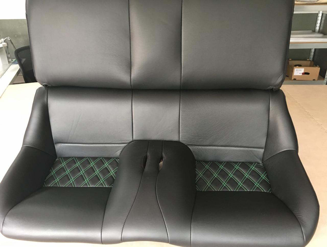 Tapicerowane, czarne skórzane siedzenie samochodowe z zielonymi przeszyciami w romby, widoczne w warsztacie tapicerskim.
