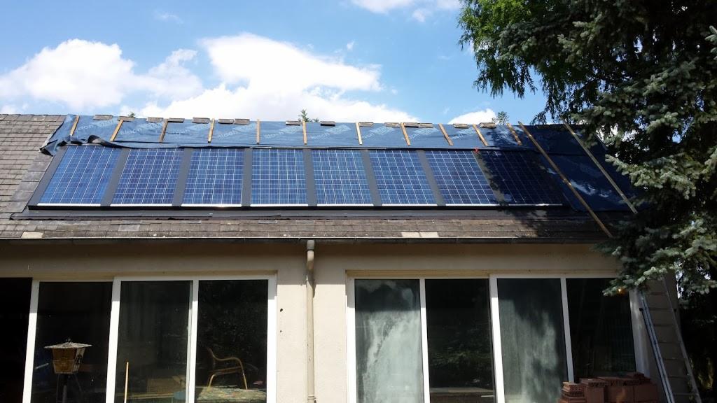 Instalacja paneli słonecznych na dachu domu jednorodzinnego, widoczne panele częściowo zamontowane, zabezpieczone folią, drabina oparta o ścianę budynku.